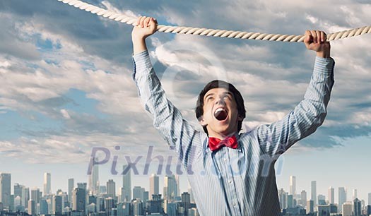 Image of businessman hanging on rope against city background Image of businessman hanging on rope against city background