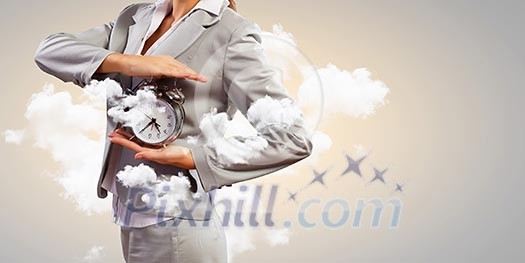 Image of young businesswoman holding alarmclock against cloudy background Image of young businesswoman holding alarmclock against cloudy background