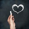 School blackboard and human hand with chalk drawing heart symbol