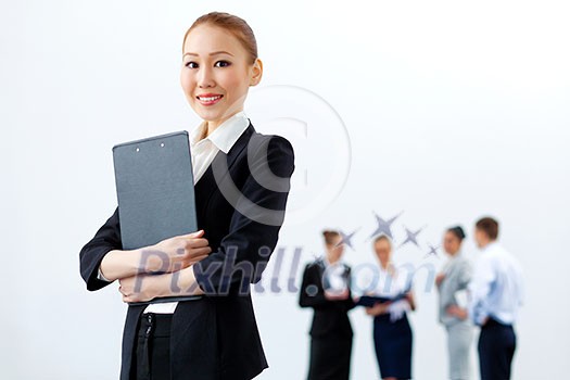 Asian young business woman holding folder with colleagues at background Asian young business woman holding folder with colleagues at background