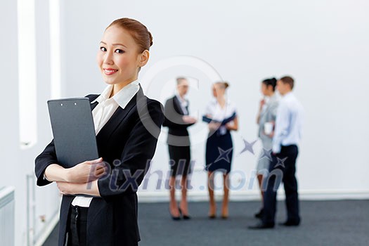 Asian young business woman holding folder with colleagues at background Asian young business woman holding folder with colleagues at background
