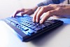 Click! Hands of a man on a keyboard with blue backlighting.