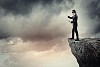 Image of businessman in blindfold standing on edge of mountain