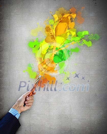 Close-up of human hand holding paint brush making colorful paint splashes Close-up of human hand holding paint brush making colorful paint splashes