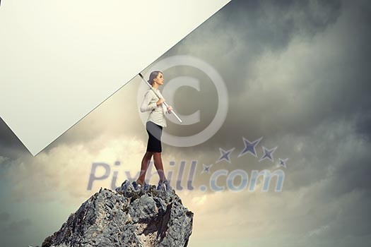 Image of business woman standing atop of hill holding blank banner Image of business woman standing atop of hill holding blank banner