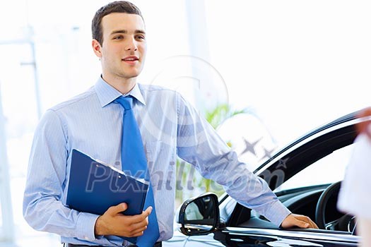 Handsome young man consultant at car salon standing near car Handsome young man consultant at car salon standing near car