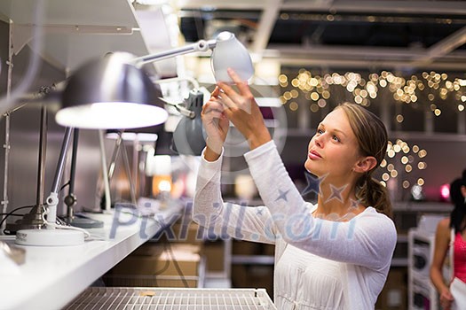 Pretty, young woman choosing the right lamp for her apartment in a modern home furnishings store (color toned image; shallow DOF) Pretty, young woman choosing the right lamp for her apartment in a modern home furnishings store (color toned image; shallow DOF)