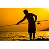 Fisherman silhouette on the beach at colorful sunset