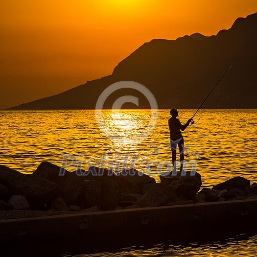 Fisherman silhouette on the beach at colorful sunset Fisherman silhouette on the beach at colorful sunset