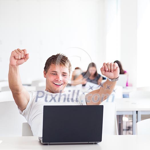 Portrait of a very happy young, male college student working on his laptop computer in a classroom/study room/library - expressing joy/success (shallow DOF; color toned image)