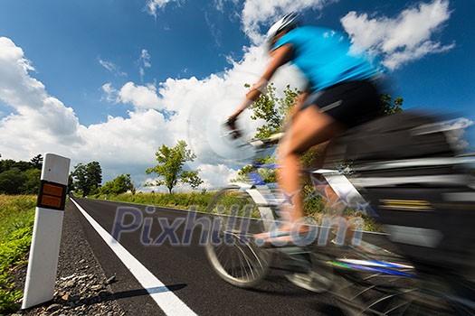 Female cyclist biking on a country road on a lovely sunny day (motion blurred image with copy space) Female cyclist biking on a country road on a lovely sunny day (motion blurred image with copy space)