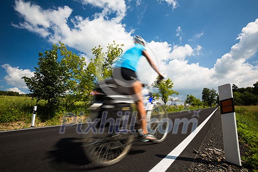 Female cyclist biking on a country road on a lovely sunny day (motion blurred image with copy space)