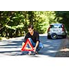 Handsome young man with his car broken down by the roadside, setting the safety triangle