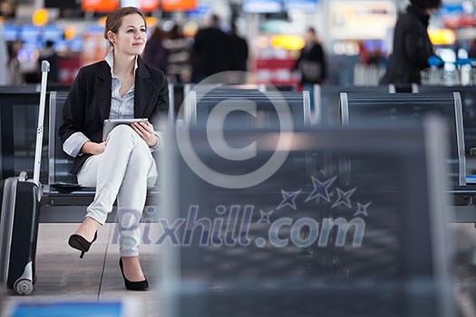 Young female passenger at the airport, using her tablet computer while waiting for her flight Young female passenger at the airport, using her tablet computer while waiting for her flight