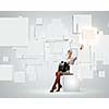 Image of elegant businesswoman sitting on white cube touching media button