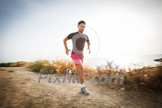 Caucasian young man running on a seacost path on a lovely summer evening, training for marathon (motion blurred image) Caucasian young man running on a seacost path on a lovely summer evening, training for marathon (motion blurred image)
