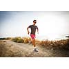 Caucasian young man running on a seacost path on a lovely summer evening, training for marathon (motion blurred image)