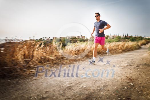 Caucasian young man running on a seacost path on a lovely summer evening, training for marathon (motion blurred image)