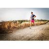 Caucasian young man running on a seacost path on a lovely summer evening, training for marathon (motion blurred image)