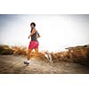 Caucasian young man running on a seacost path on a lovely summer evening, training for marathon (motion blurred image)