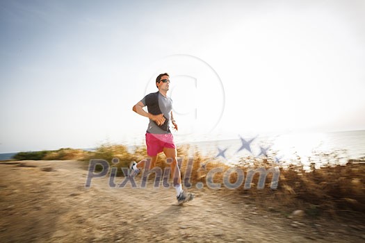 Caucasian young man running on a seacost path on a lovely summer evening, training for marathon (motion blurred image)