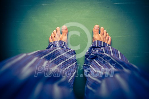 Alone in the house: man in pyjamas looking down on his bare feet Alone in the house: man in pyjamas looking down on his bare feet