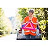 Young female driver wearing a high visibility vest, setting up the reflective trianglec after her car has broken down