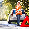 Young female driver wearing a high visibility vest, calling the roadside service/assistance after her car has broken down