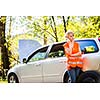 Young female driver wearing a high visibility vest, calling the roadside service/assistance after her car has broken down