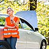 Young female driver wearing a high visibility vest, calling the roadside service/assistance after her car has broken down