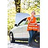 Young female driver wearing a high visibility vest, calling the roadside service/assistance after her car has broken down