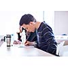 young, handsome male college student sitting in a classroom full of students during class (color toned image; shallow DOF)
