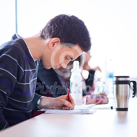 young, handsome male college student sitting in a classroom full of students during class (color toned image; shallow DOF) young, handsome male college student sitting in a classroom full of students during class (color toned image; shallow DOF)