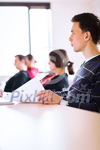 young, handsome male college student sitting in a classroom full of students during class (color toned image; shallow DOF) young, handsome male college student sitting in a classroom full of students during class (color toned image; shallow DOF)