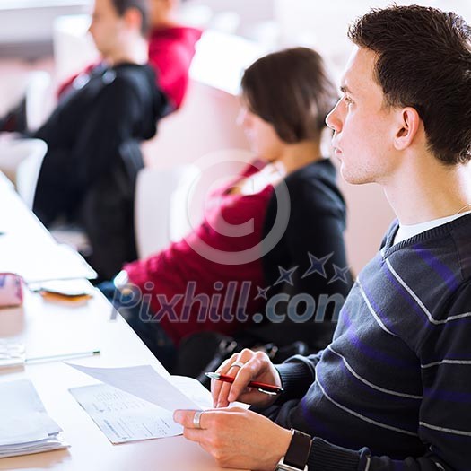 young, handsome male college student sitting in a classroom full of students during class (color toned image; shallow DOF) young, handsome male college student sitting in a classroom full of students during class (color toned image; shallow DOF)