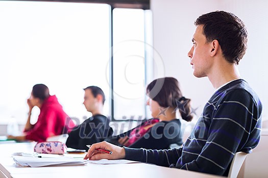 young, handsome male college student sitting in a classroom full of students during class (color toned image; shallow DOF) young, handsome male college student sitting in a classroom full of students during class (color toned image; shallow DOF)