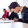 young, handsome male college student sitting in a classroom full of students during class (color toned image; shallow DOF)