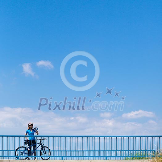 Background for poster or advertisment pertaining to cycling/sport/outdoor activities - female cyclist during a halt on a bridge against blue sky (color toned image) Background for poster or advertisment pertaining to cycling/sport/outdoor activities - female cyclist during a halt on a bridge against blue sky (color toned image)