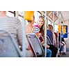 Pretty, young woman on a streetcar/tramway, during her commute to work/school (color toned image; shallow DOF)