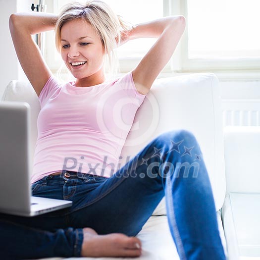Pretty young woman using her laptop while relaxing on a sofa at home§ Pretty young woman using her laptop while relaxing on a sofa at home§