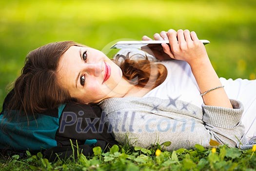 Young woman using her tablet computer while relaxing outdoors in a park on a lovely spring day Young woman using her tablet computer while relaxing outdoors in a park on a lovely spring day