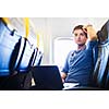 Handsome young man daydreaming while working on his laptop computer on board of an airplane during flight