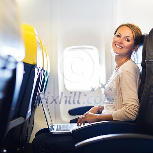 Young woman working on her laptop computer on board of an airplane during the flight Young woman working on her laptop computer on board of an airplane during the flight
