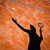 shadow of a tennis player in action on a tennis court (conceptual image with a tennis ball lying on the court and the shadow of the player positioned in a way he seems to be playing it)