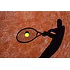 shadow of a tennis player in action on a tennis court (conceptual image with a tennis ball lying on the court and the shadow of the player positioned in a way he seems to be playing it)