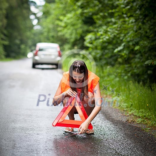 Young female driver wearing a high visibility vest, calling the roadside service/assistance after her car has broken down Young female driver wearing a high visibility vest, calling the roadside service/assistance after her car has broken down