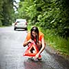 Young female driver wearing a high visibility vest, calling the roadside service/assistance after her car has broken down