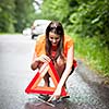 Young female driver wearing a high visibility vest, calling the roadside service/assistance after her car has broken down