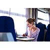 Young woman using her laptop computer while on the train (shallow DOF; color toned image)