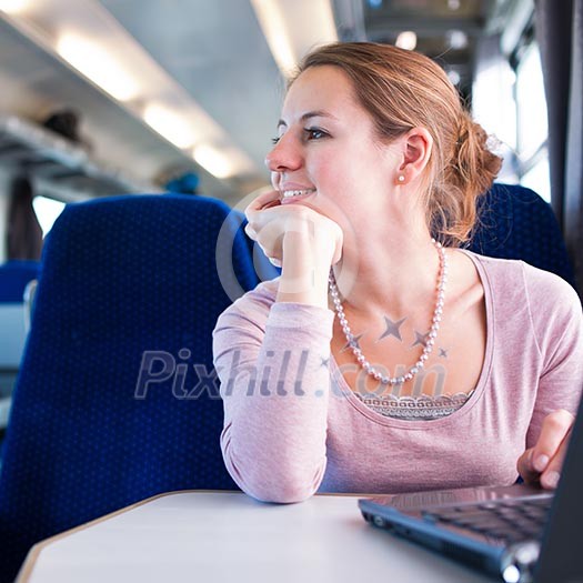 Young woman using her laptop computer while on the train (shallow DOF; color toned image)